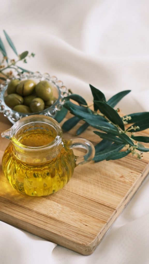 Close-up of olive oil and olives with leaves on a wooden cutting board.